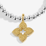 Close-up of the textured gold-plated flower charm on a Joma bracelet