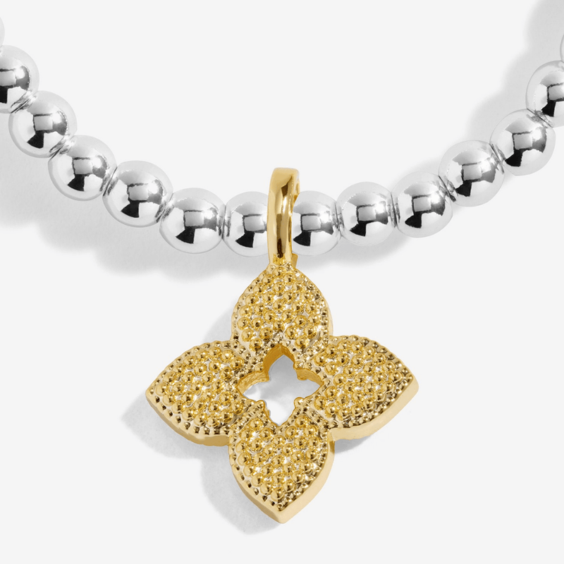 Close-up of the textured gold-plated flower charm on a Joma bracelet