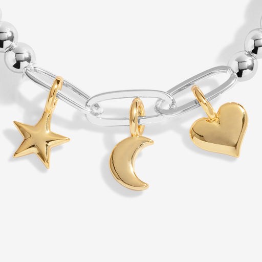 Close‑up of petite gold star, crescent‑moon and heart charms hanging from silver paper‑clip links.
