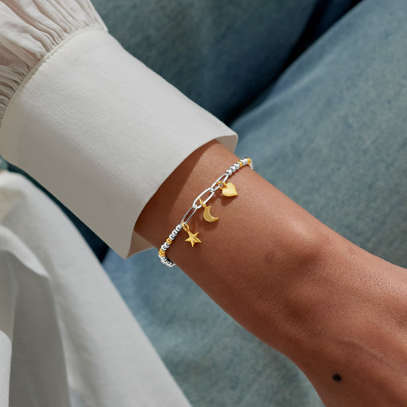 Celestial charm bracelet styled on wrist, showing alternating silver‑gold beads and dangling gold icons.