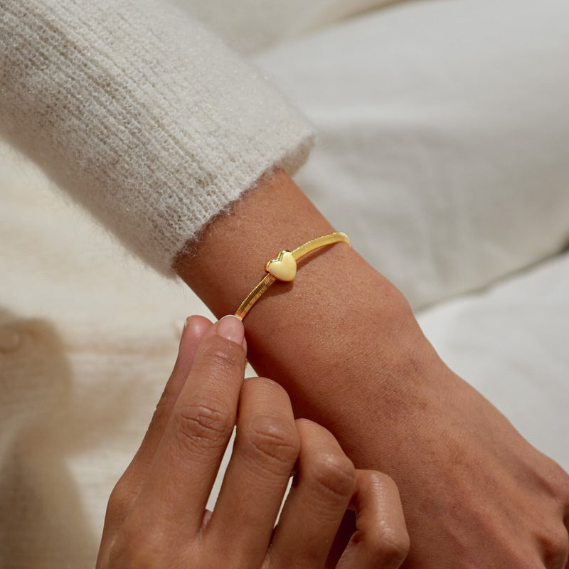 Gold heart slider bracelet styled on wrist, sleek herringbone chain with adjustable slider for a perfect fit.

