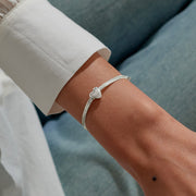 Silver heart slider bracelet styled on wrist, showing smooth herringbone chain and slider for a custom fit.
