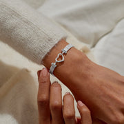 Silver mesh heart‑clasp bracelet styled on wrist, highlighting its sleek texture and statement closure.

