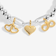Close‑up of the polished gold heart, infinity and double‑heart charms hanging from silver paper‑clip links.
