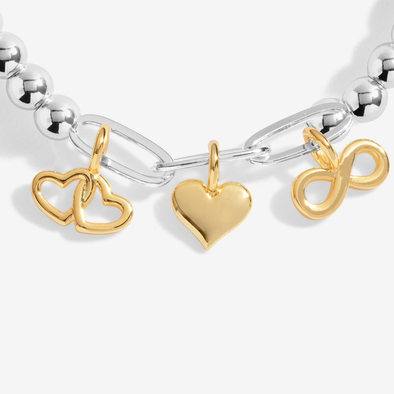 Close‑up of the polished gold heart, infinity and double‑heart charms hanging from silver paper‑clip links.
