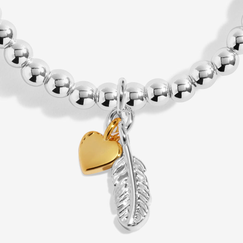 Close-up of silver feather charm and gold heart charm on silver beaded stretch Bracelet