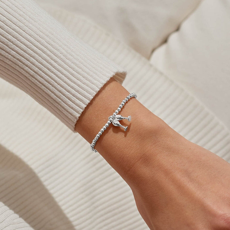 “Christmas Cheers” bracelet styled on wrist – sparkling clinking flutes charm adds celebration sparkle to holiday outfits.
