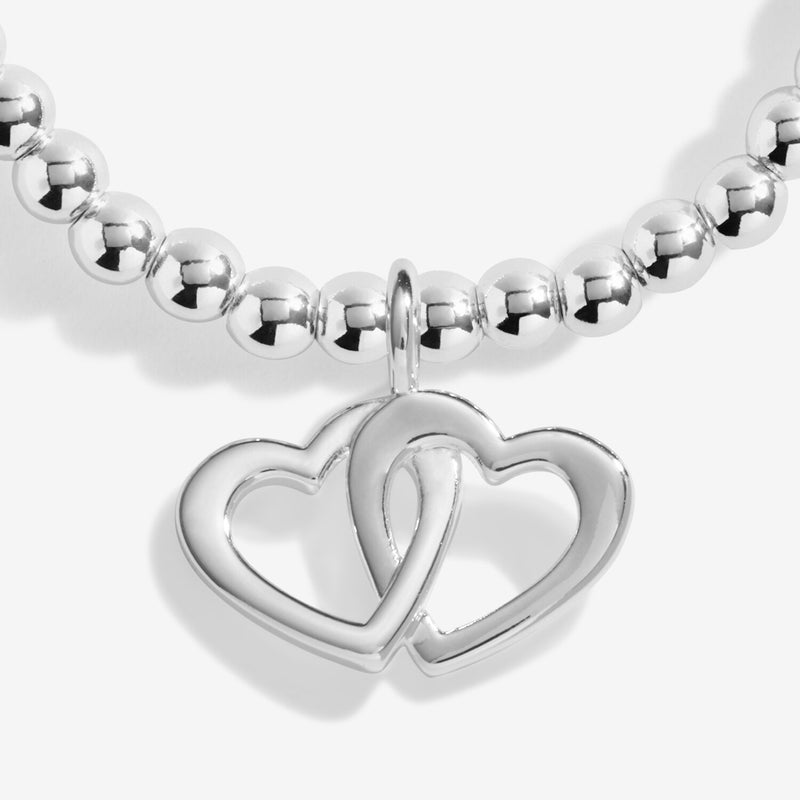 Highly polished interlocking open‑heart pendant hanging from petite silver beads on the Fabulous Friend stretch bracelet.
