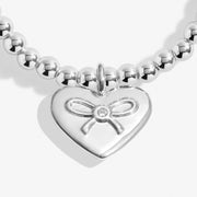 Close‑up of polished heart charm with ribbon bow and tiny crystal centre on Joma Jewellery auntie Christmas bracelet.
