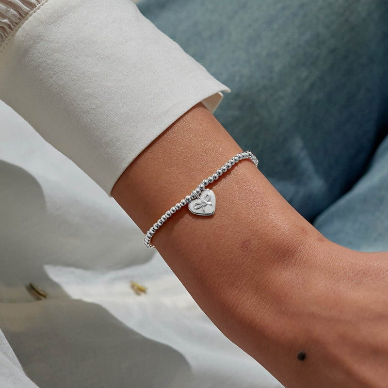 Sparkling Auntie Christmas bracelet styled on wrist – delicate sterling silver beaded band and festive heart bow charm.
