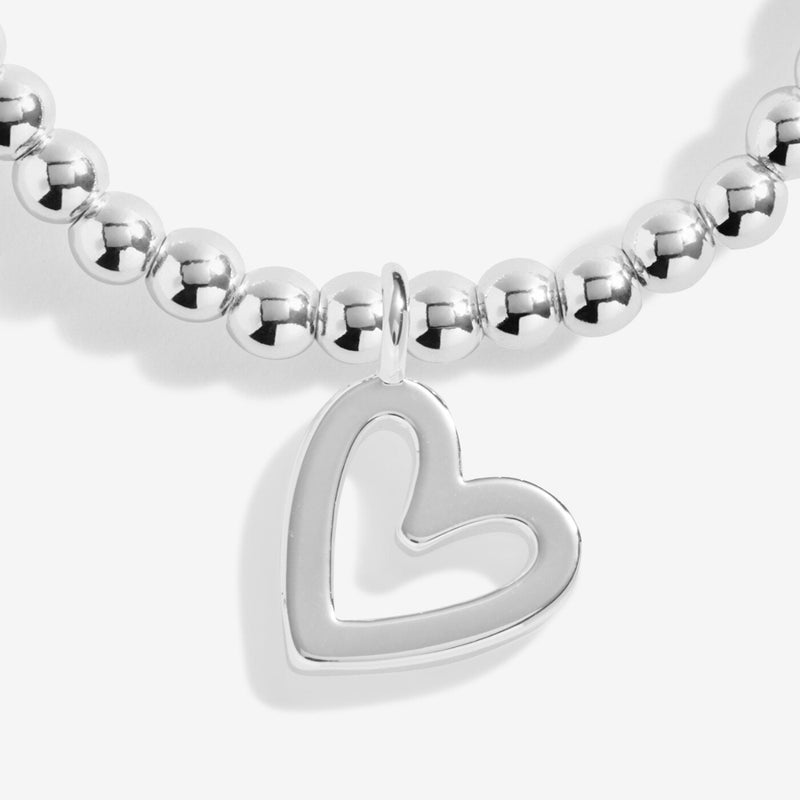 Close‑up of polished open‑heart pendant hanging from petite round silver beads on stretchy bracelet.
