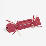 Red cracker‑style gift box with ribbon presenting Joma Jewellery Merry Christmas open‑heart bracelet.