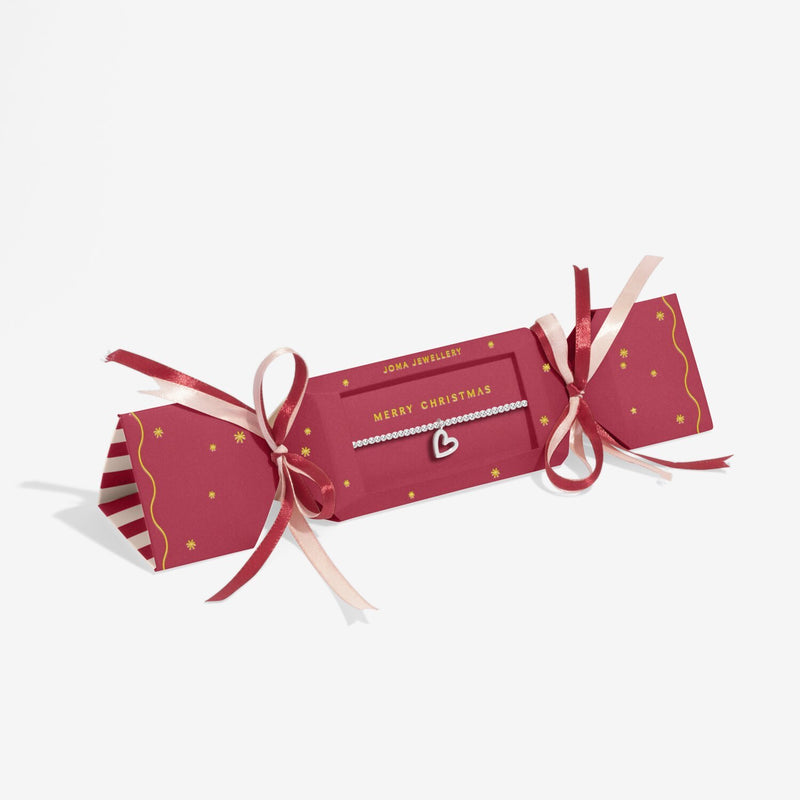 Red cracker‑style gift box with ribbon presenting Joma Jewellery Merry Christmas open‑heart bracelet.