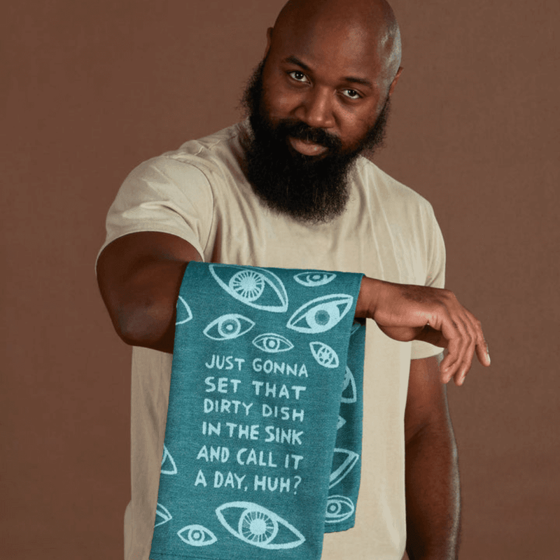 Model holding teal woven tea towel with eye pattern and dirty dish in the sink slogan.
