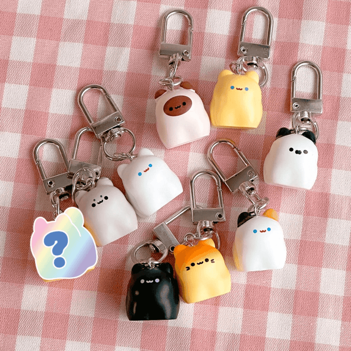 Kawaii Bread Cat Keychain Mystery Blind Box flat lay showing assorted pastel cat keyrings on pink gingham fabric