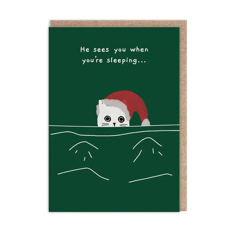 Dark green Christmas card with a white cat in a Santa hat peeking over a duvet; text reads He sees you when you’re sleeping; A6, blank inside, brown kraft envelope by Ken The Cat