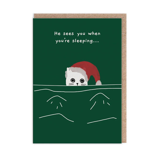 Dark green Christmas card with a white cat in a Santa hat peeking over a duvet; text reads He sees you when you’re sleeping; A6, blank inside, brown kraft envelope by Ken The Cat