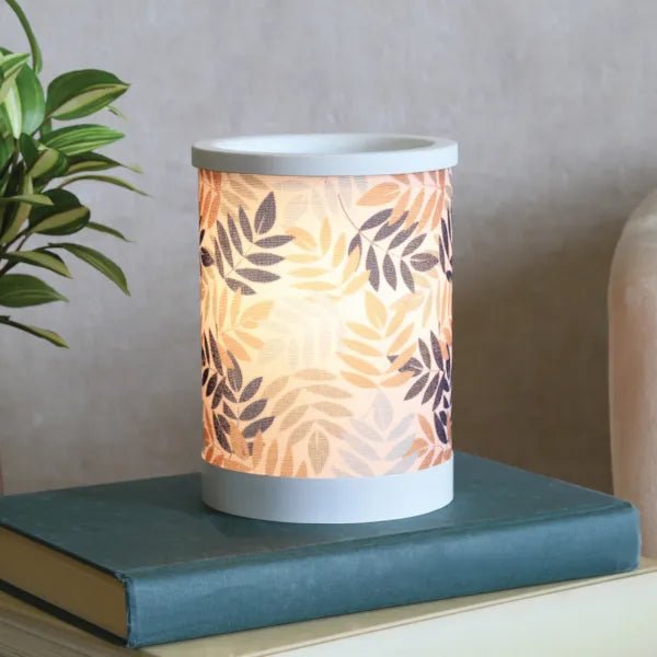 Leaves electric wax melt burner lit in a styled setting, glowing on a blue book next to a houseplant.