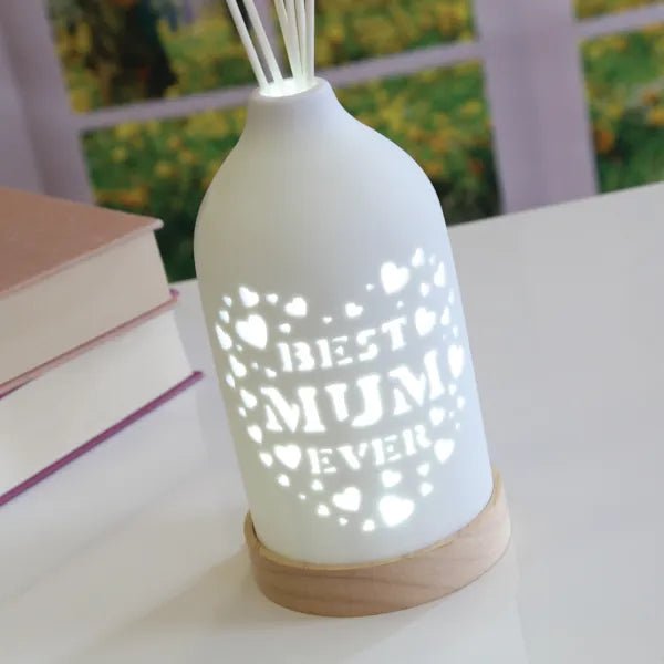 Best Mum LED ceramic reed diffuser glowing in a styled setting on a tabletop next to stacked books.