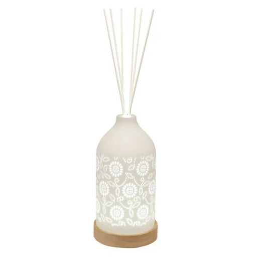 White ceramic floral reed diffuser on a wooden base with white reeds in place.