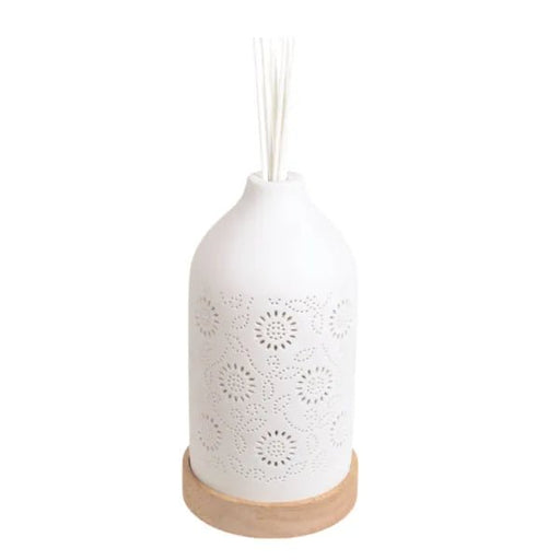 Assembled white ceramic floral reed diffuser with reeds standing on a wooden base.