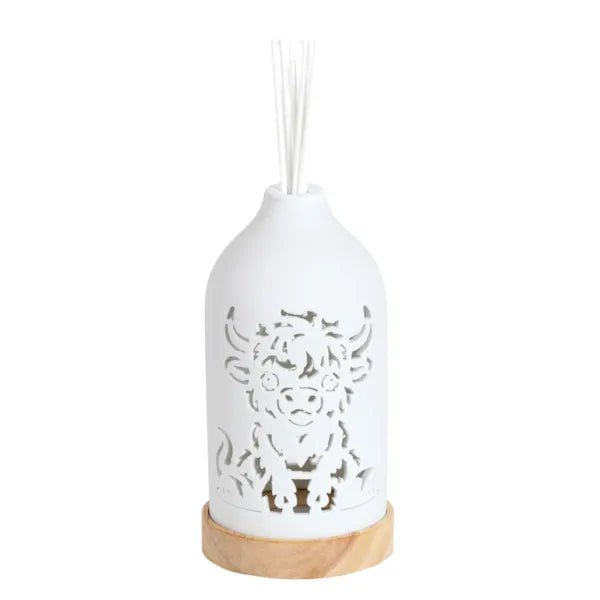 White ceramic Highland cow reed diffuser assembled on a wooden base with reed sticks in place.