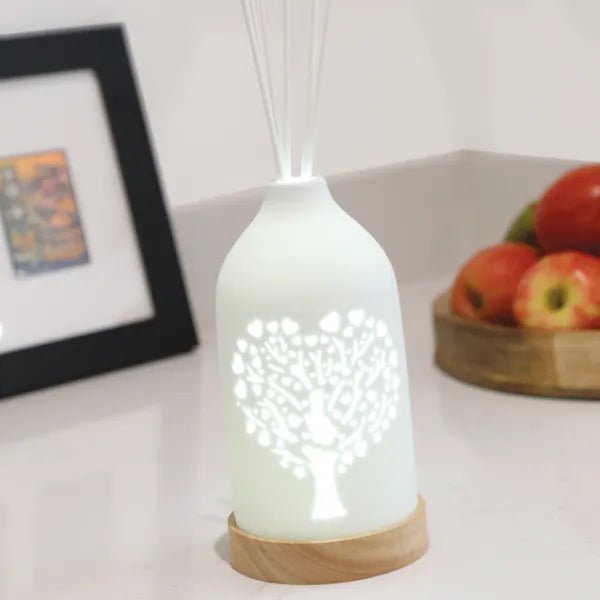 Heart tree LED reed diffuser glowing on white countertop next to fruit bowl


