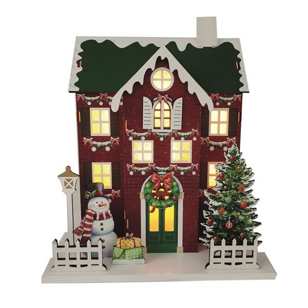Wooden red townhouse with green roof and wreath, lit windows and snowman, 24 x 24cm, on white background.