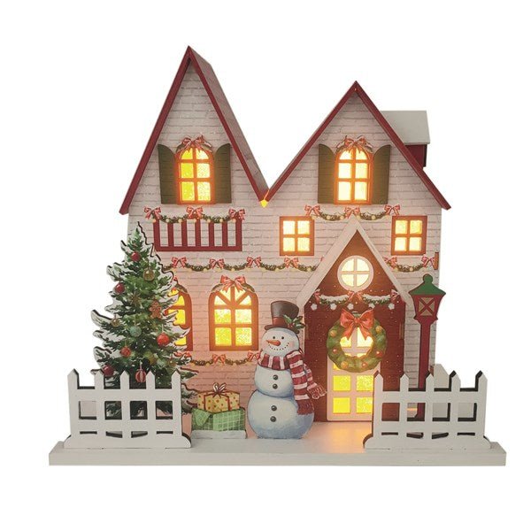 White wooden Christmas house with red roof, lit windows, wreath, tree and snowman, 24 x 22cm, on white background.