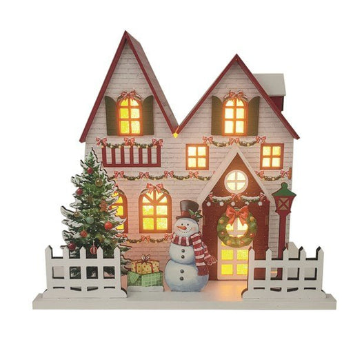 White wooden Christmas house with red roof, lit windows, wreath, tree and snowman, 24 x 22cm, on white background.