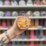 Lemon Fizzy wax melt pot held in hand with colourful wax melt display in the background