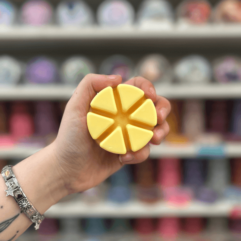Lemon Fizzy wax melt segments held in hand with colourful wax melt display in the background