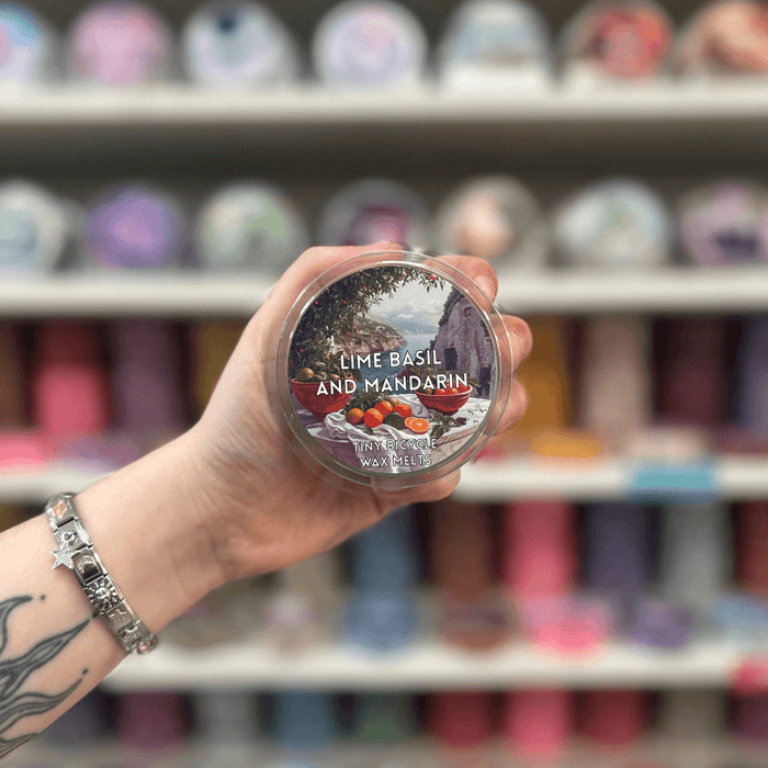 Lime Basil and Mandarin wax melt pot held in hand with colourful wax melt display in the background