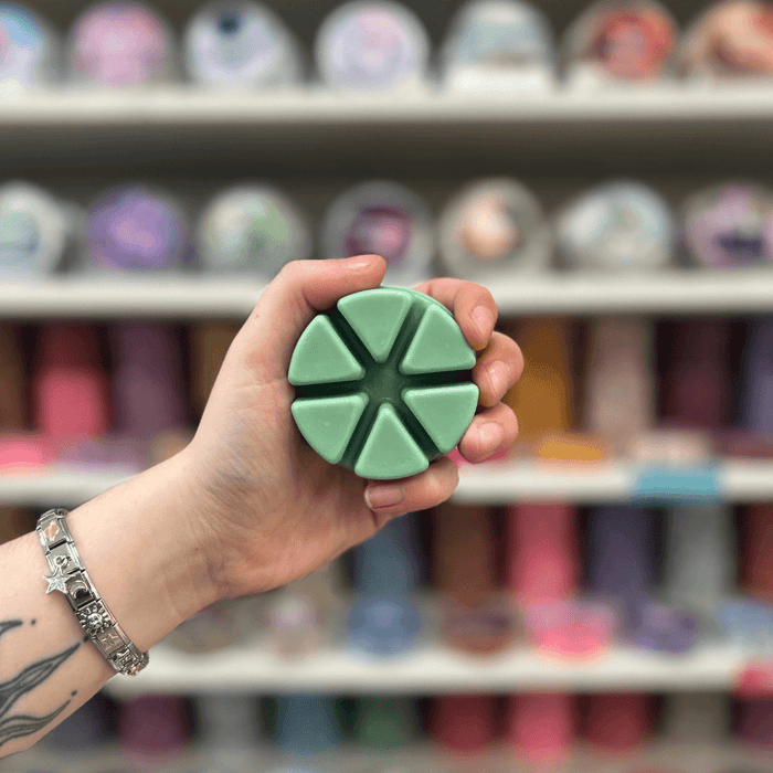 Lime Basil and Mandarin wax melt segments held in hand with colourful wax melt display in the background