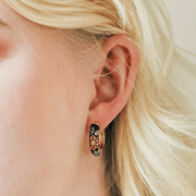 Close-up of a black cloisonné floral hoop earring being worn
