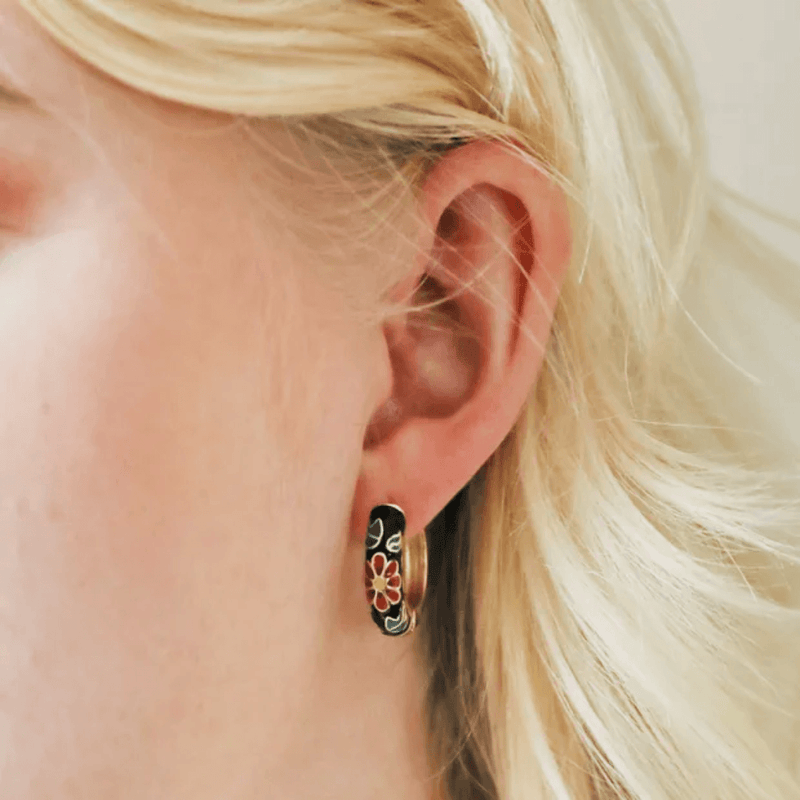 Close-up of a black cloisonné floral hoop earring being worn