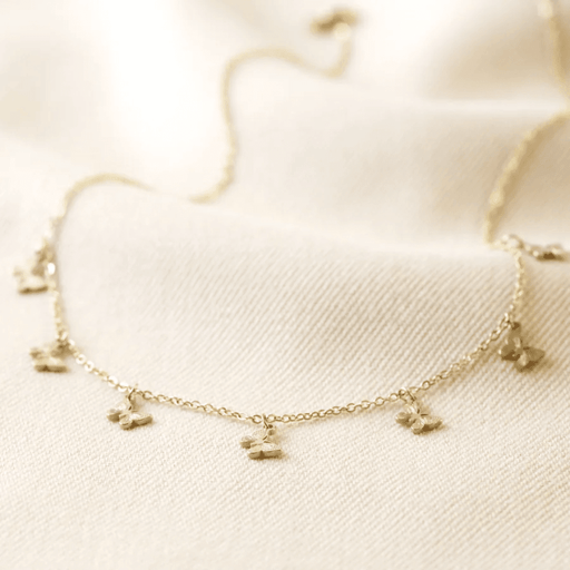 Macro shot of gold plated stainless steel butterfly charm necklace showing textured butterfly charms and fine trace chain.