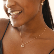 Lifestyle photo of model wearing a gold sun and moon charm necklace with sparkling cubic zirconia details.