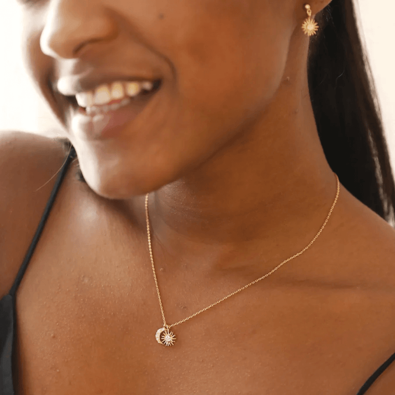 Lifestyle photo of model wearing a gold sun and moon charm necklace with sparkling cubic zirconia details.