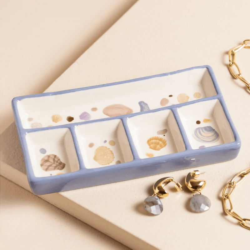 Blue and white ceramic trinket tray with shell illustrations and five compartments, styled with gold jewellery and earrings.