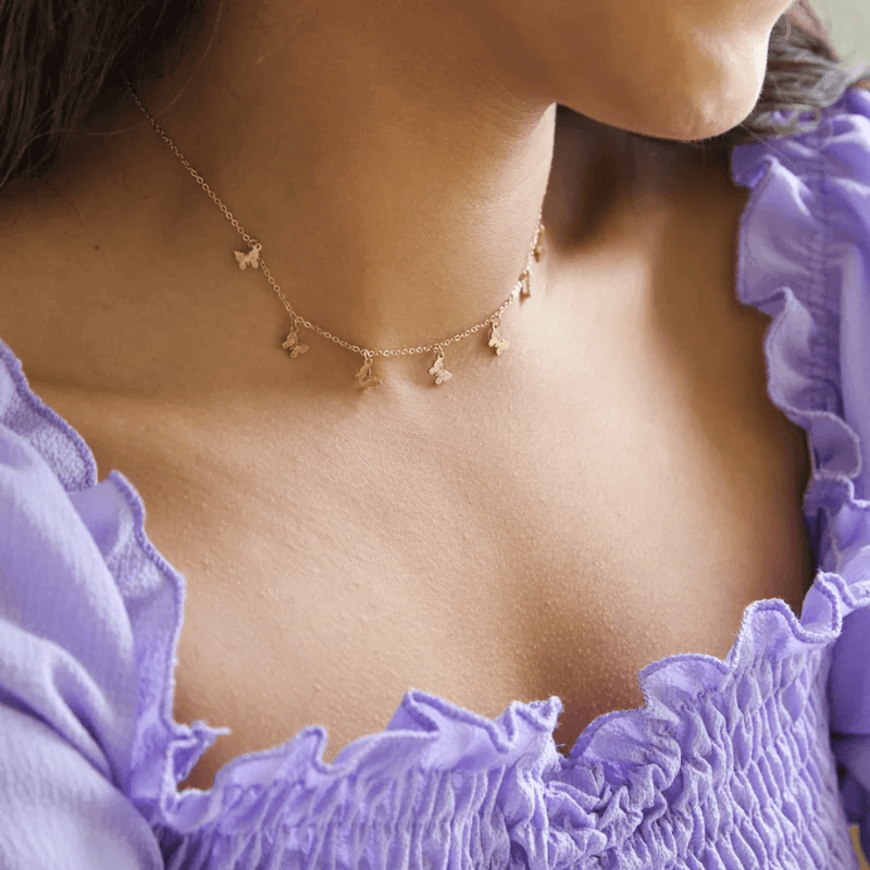 Gold butterfly charm necklace worn on the neck, showing seven small butterfly charms on a delicate chain.