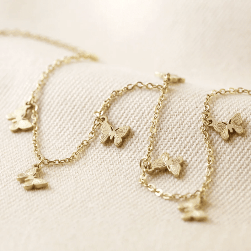 Close-up of gold plated stainless steel butterfly charm necklace with seven tiny butterfly charms on a delicate trace chain.