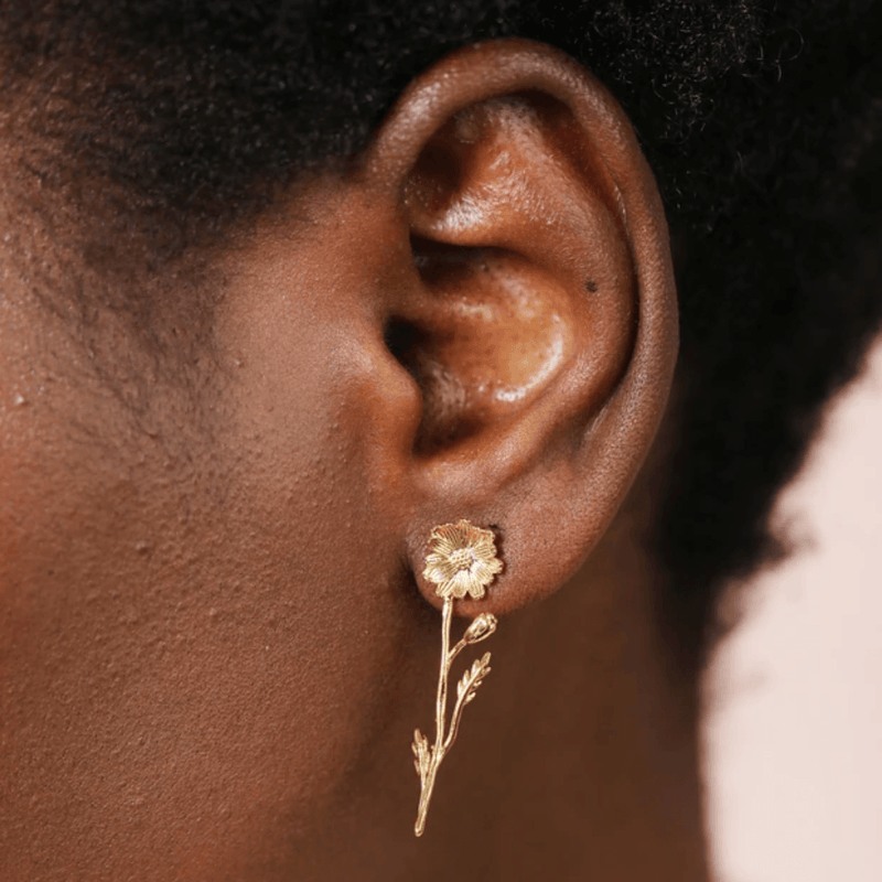 Close-up of a Lisa Angel gold flower and stem drop earring being worn