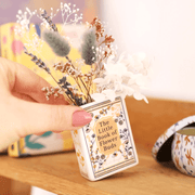 Hand holding the Lisa Angel Little Book of Flower Buds tiny ceramic vase with dried flowers