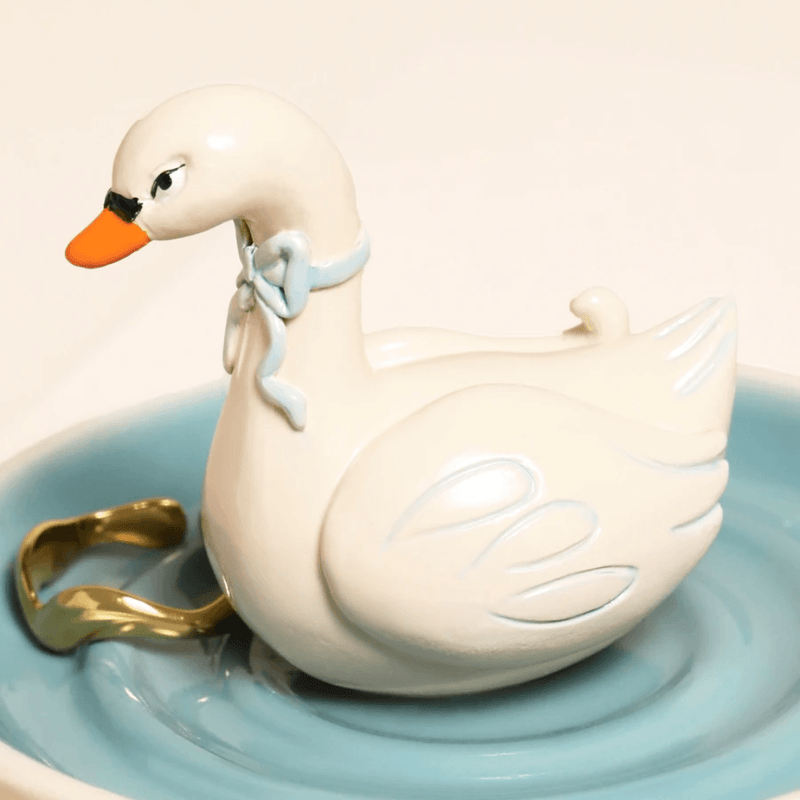 Close up of Lisa Angel swan ring holder and blue trinket dish with gold jewellery