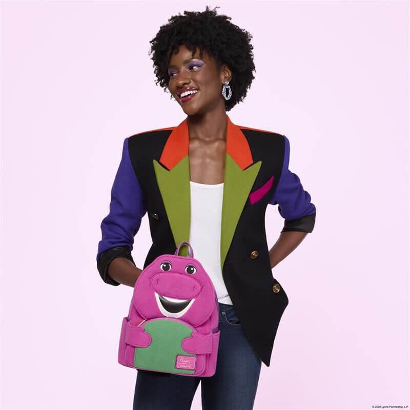Model holding the Loungefly Barney mini backpack featuring Barney’s smiling face in plush purple with a green tummy pocket.