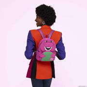 Model wearing the Loungefly Barney mini backpack on the back, showing the compact size, purple straps and character face front.