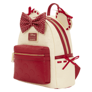 Angled view of the Loungefly Disney Minnie Mouse mini backpack showing the red polka dot bow, gold zip, cream body and red front pocket.