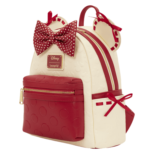 Angled view of the Loungefly Disney Minnie Mouse mini backpack showing the red polka dot bow, gold zip, cream body and red front pocket.