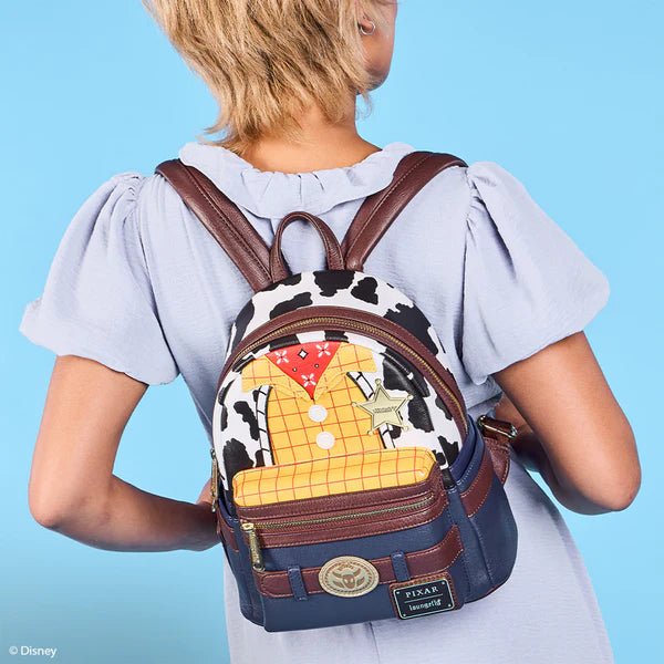 Model wearing Loungefly Toy Story Woody backpack against blue backdrop, showing cow print and sheriff badge detail
